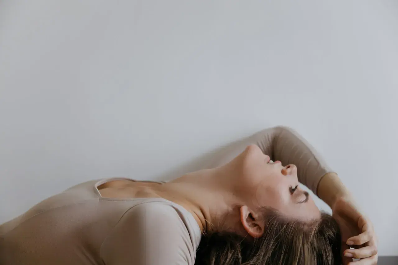Kobieta w beżowym body, z głową odrzuconą do tyłu, w geście przypominającym sensate focus.