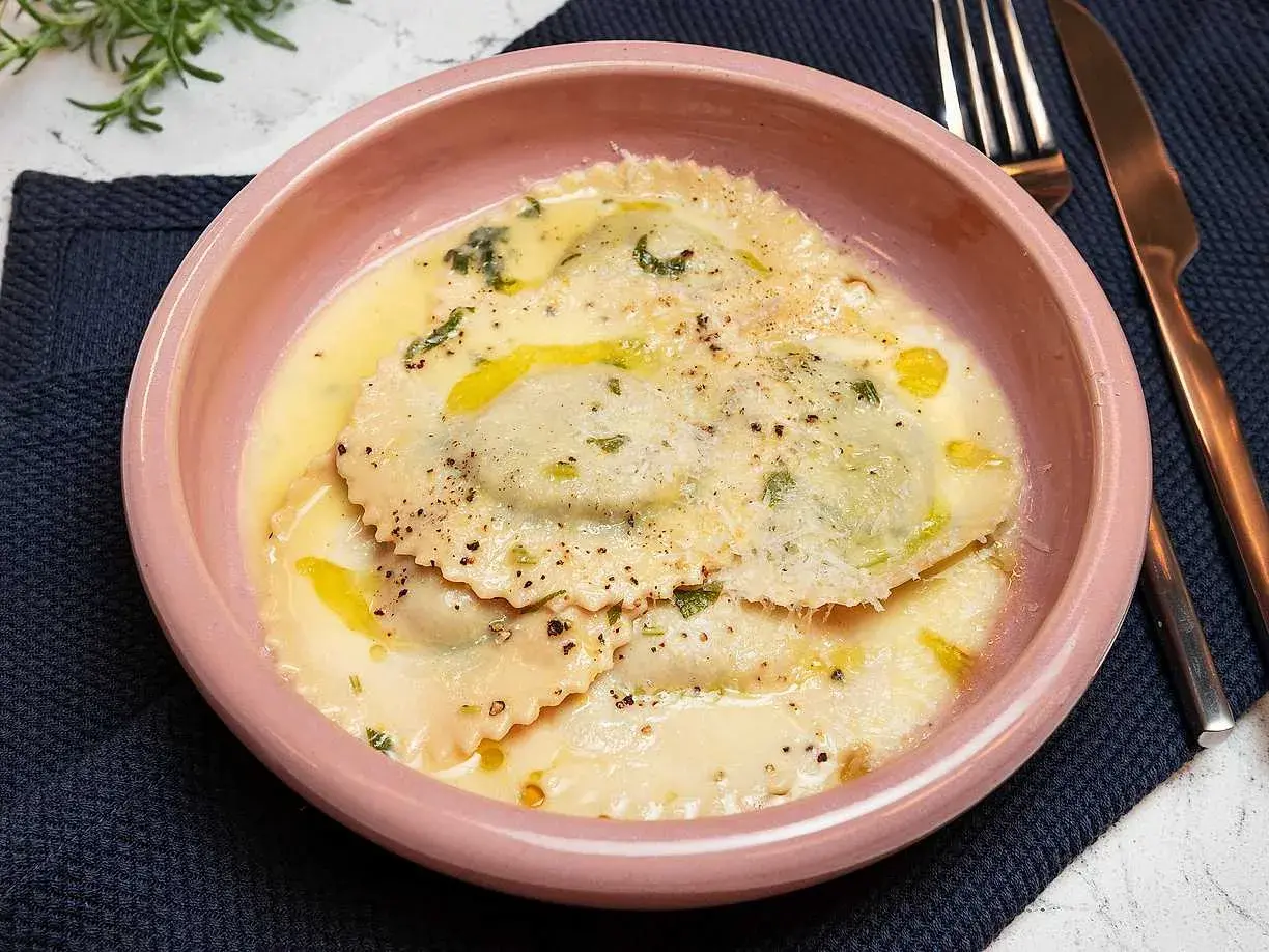 En skål med krämig ravioli, perfekt för ett enkelt ravioli recept. Garnerad med örter och parmesan.
