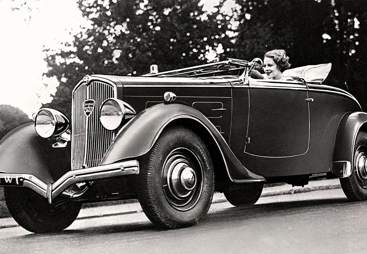 En kvinna kör en elegant cabriolet, ett exempel på gamla bilmodeller från 1930-talet.