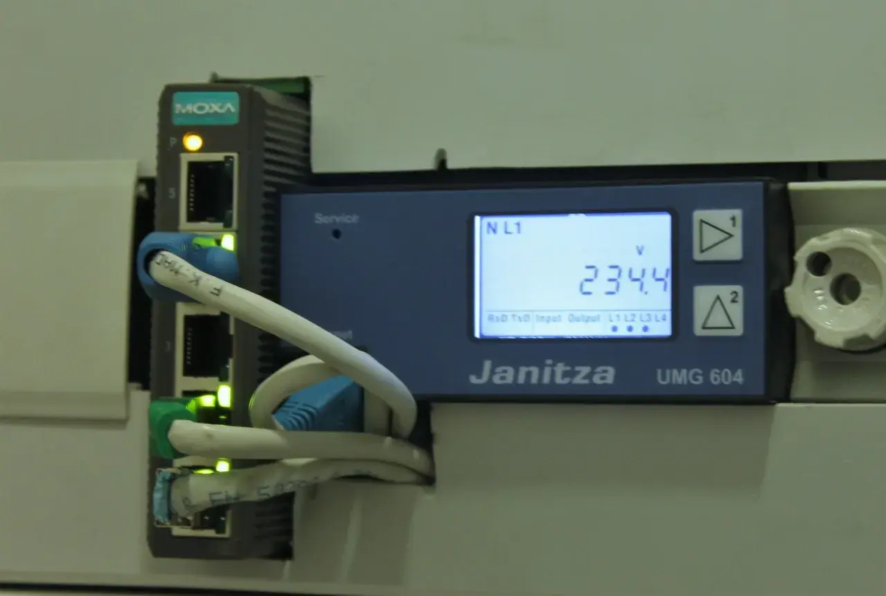 Urządzenie Janitza UMG 604 z modułem MOXA zbiera dane, umożliwiając telemetrię. Na ekranie widoczny pomiar napięcia 234.4V.