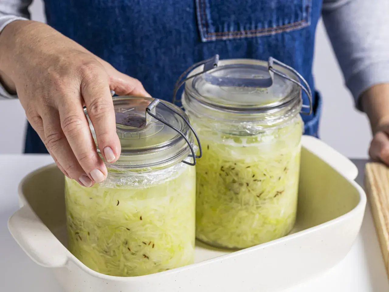 Hände setzen zwei Gläser mit Sauerkraut zum Fermentieren in ein Gefäß.