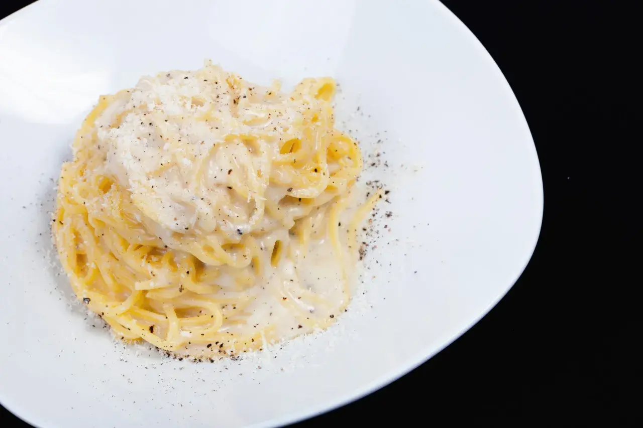 Pici cacio e pepe, un classico piatto di pasta romana, servito su un piatto bianco con abbondante pepe nero macinato e formaggio grattugiato.