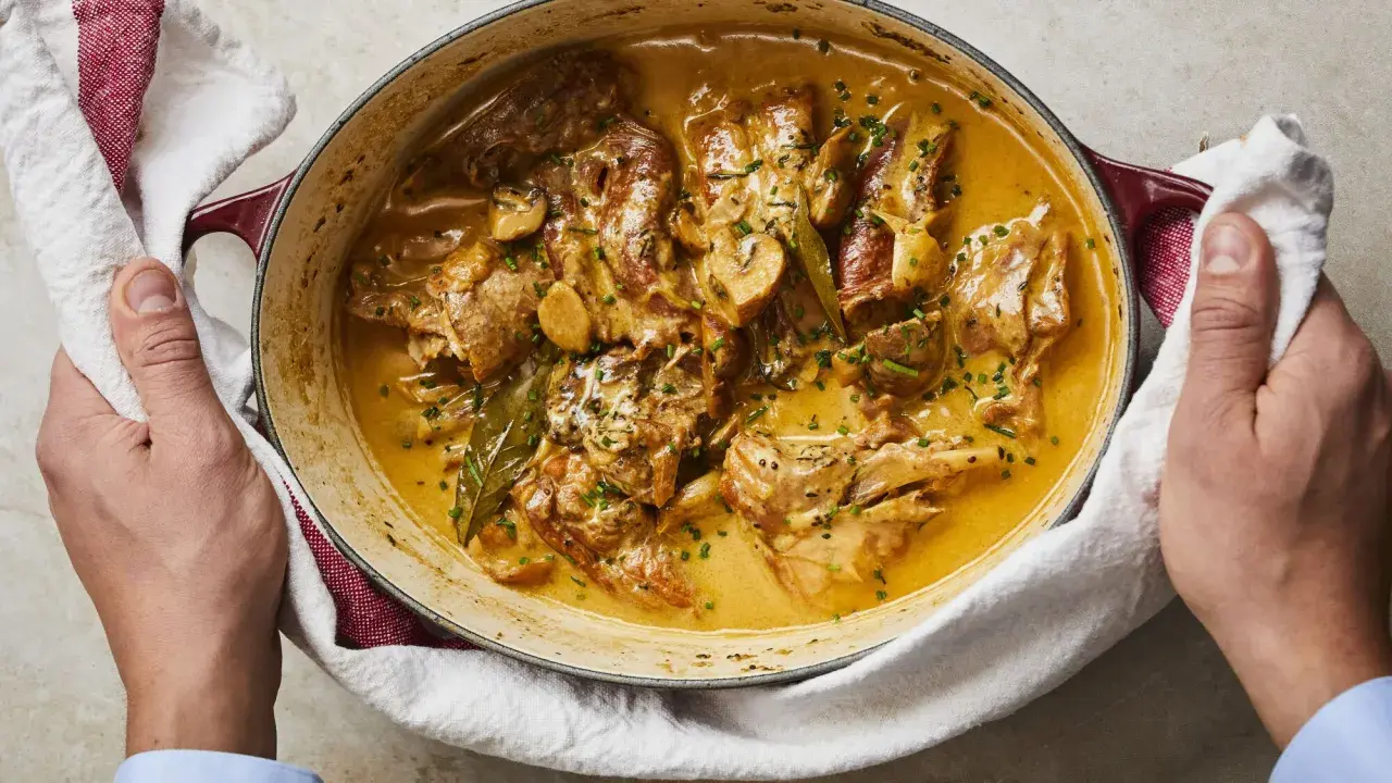 Un plat de lapin à la moutarde crémeuse, garni de persil frais et de champignons, servi dans une cocotte en fonte.