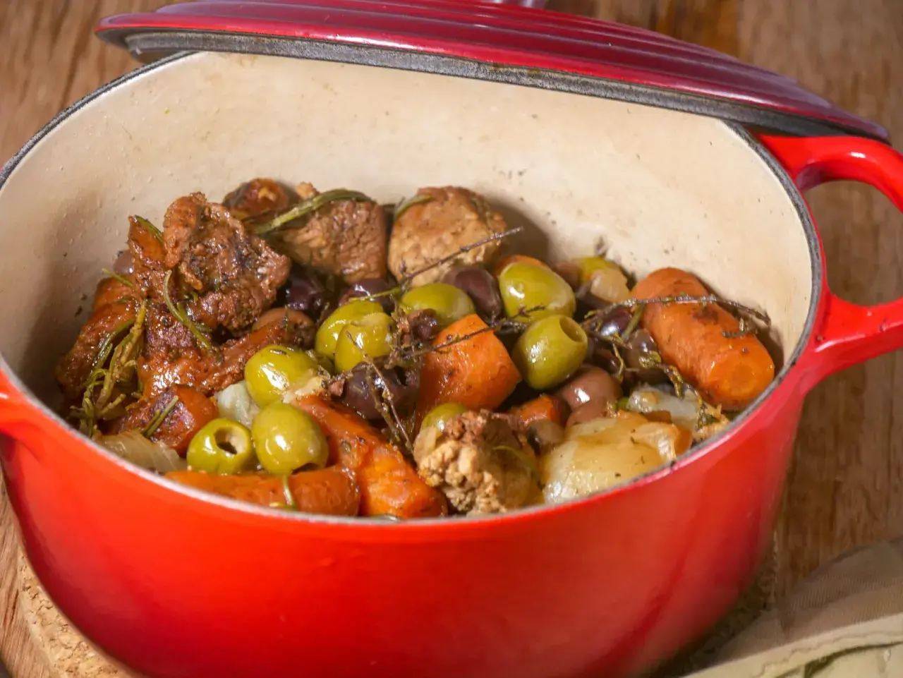 Un savoureux sauté de veau aux olives, carottes et herbes aromatiques mijote dans une cocotte rouge.