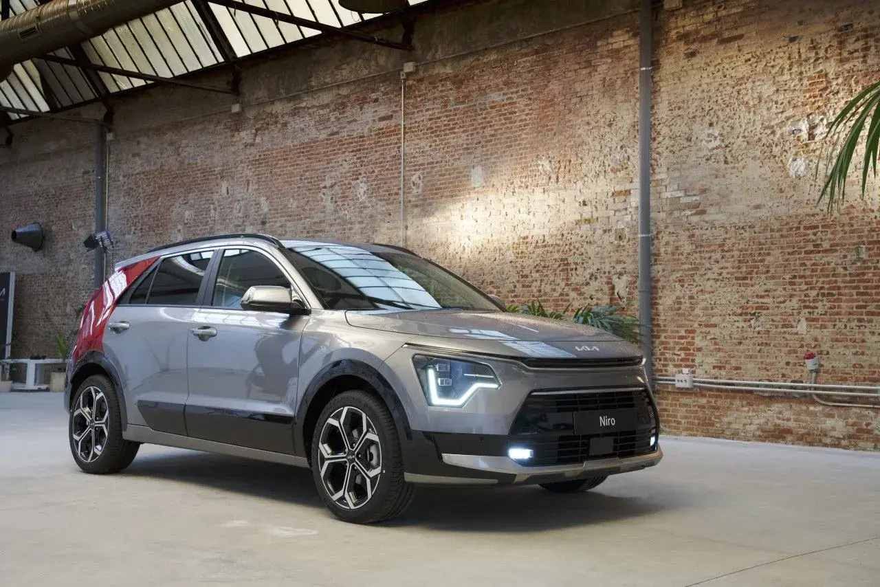 Un Kia Niro gris con detalles rojos en el pilar C, listo para una prueba. El coche está en un interior con paredes de ladrillo y techo acristalado.