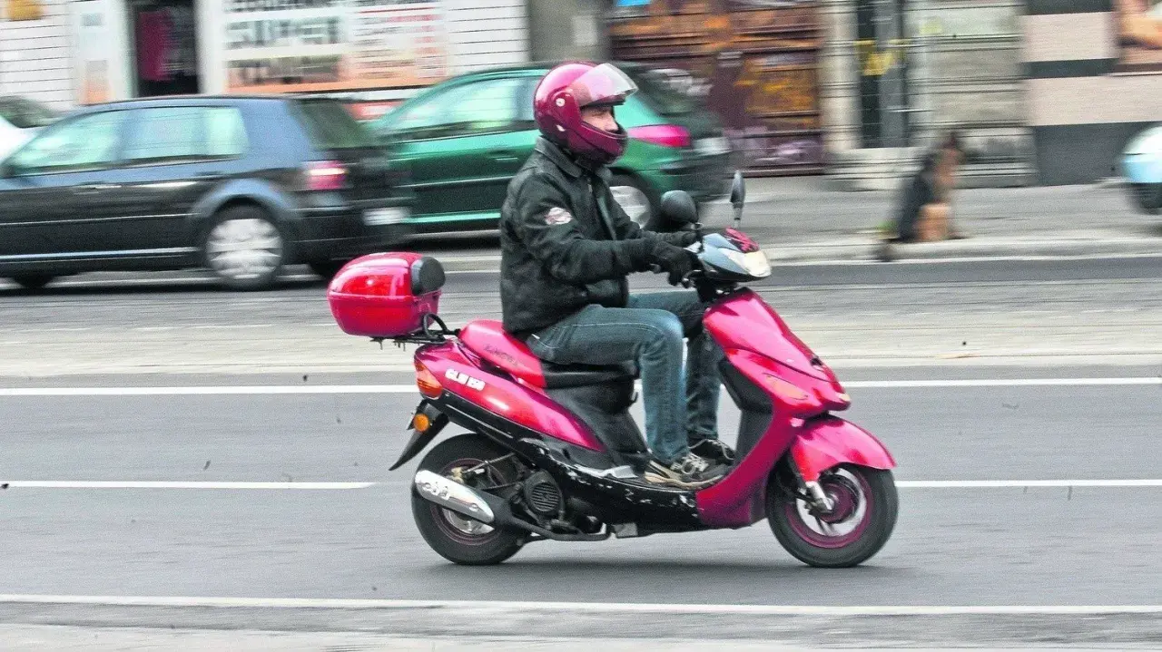 Mężczyzna w kasku jedzie na różowym skuterze. Czy z kartą rowerową można jeździć na skuterze? To pytanie nurtuje wielu.