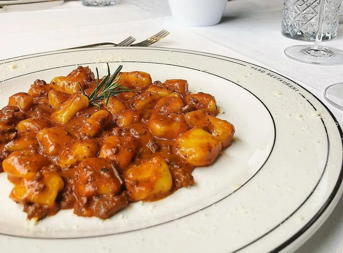 Gnocchi al ragù, un classico tra i piatti tipici maceratesi, serviti su un piatto bianco con rosmarino fresco.