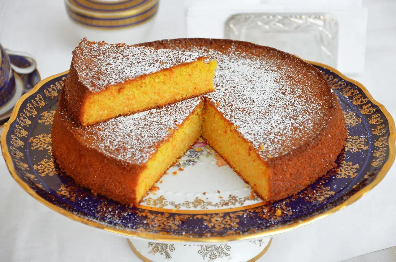 Una deliziosa torta carote e mandorle, spolverata di zucchero a velo, servita su un elegante piatto decorato.