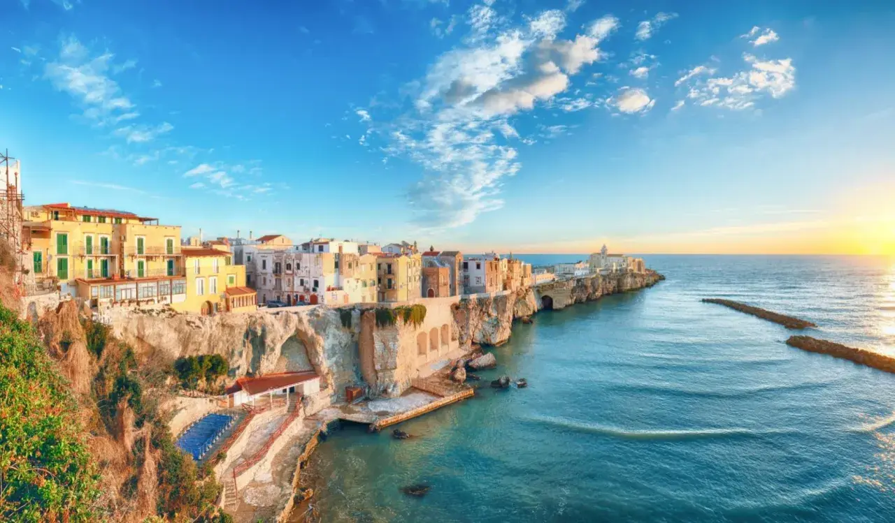 San Mennaio, un borgo sul mare con case colorate aggrappate alla scogliera, baciato dal sole al tramonto.