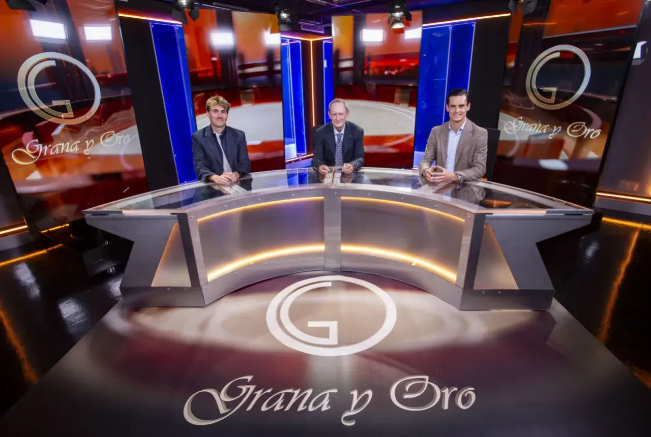 Tres hombres sentados en un plató de televisión con el logo "Grana y Oro" en el fondo y en el suelo.