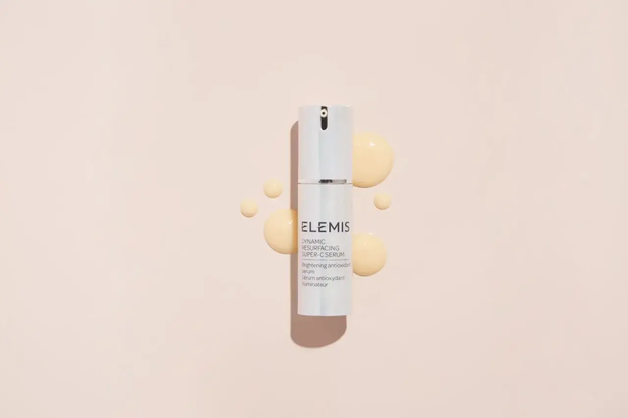Siero ELEMIS con acido glicolico e vitamina C, per una pelle luminosa e rinnovata, circondato da gocce dorate.