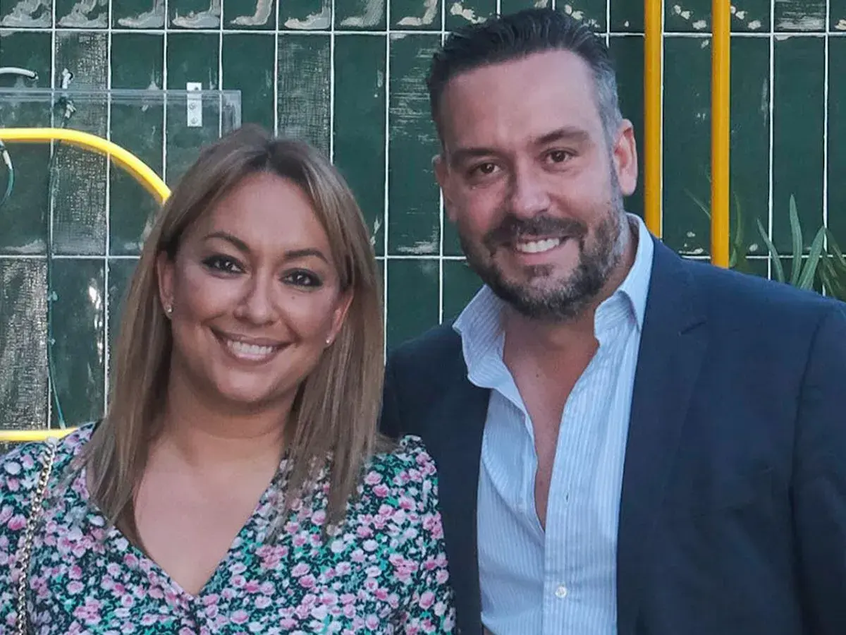 Kike Calleja y su pareja sonríen a la cámara. Ella lleva un vestido floral y él un traje azul.