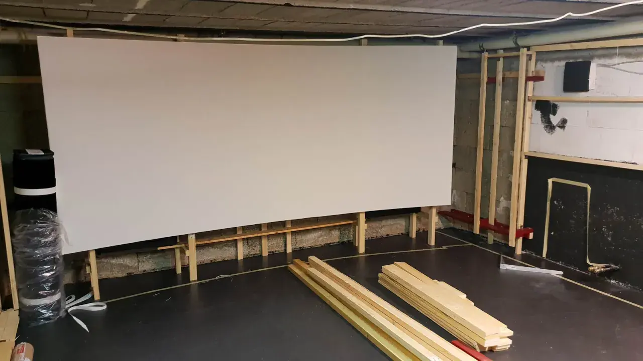 Große, weiße Leinwand für ein Heimkino, gestützt von Holzrahmen. Material für den **Beamer Leinwand selber bauen** liegt bereit.