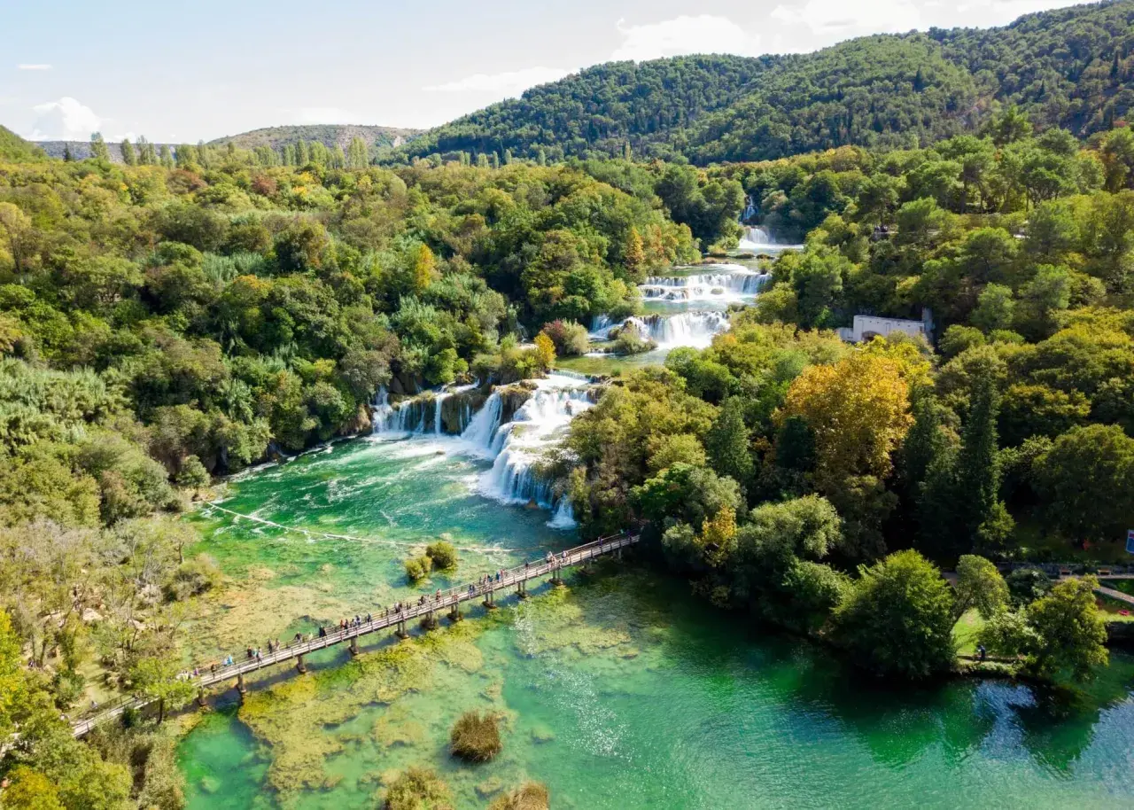 Atemberaubende Wasserfälle im Krka Nationalpark, Kroatien. Eine Holzbrücke führt Besucher über das smaragdgrüne Wasser.