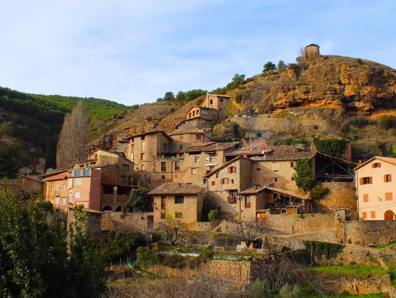 Un pintoresco senet de Barrabés se aferra a la ladera, con casas de piedra y tejados de teja bajo un cielo azul.
