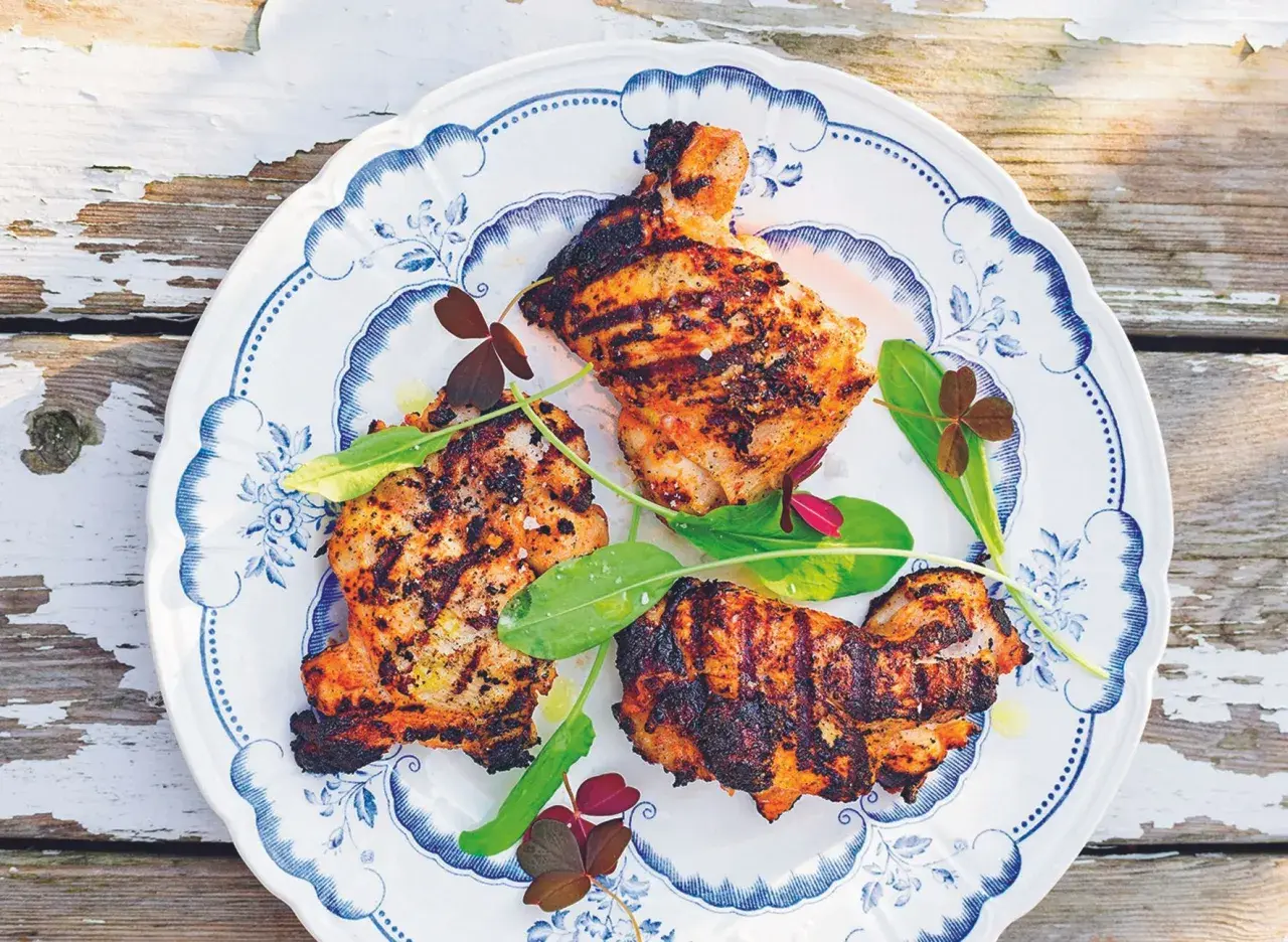 Grillad yoghurtmarinerad kyckling med gröna blad och klöver på en blåvit tallrik.