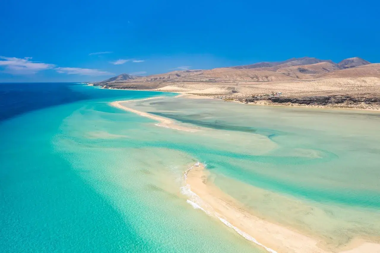 Aguas turquesas y arena dorada en Fuerteventura. Un paraíso natural para descubrir qué ver en Fuerteventura, con montañas áridas al fondo.