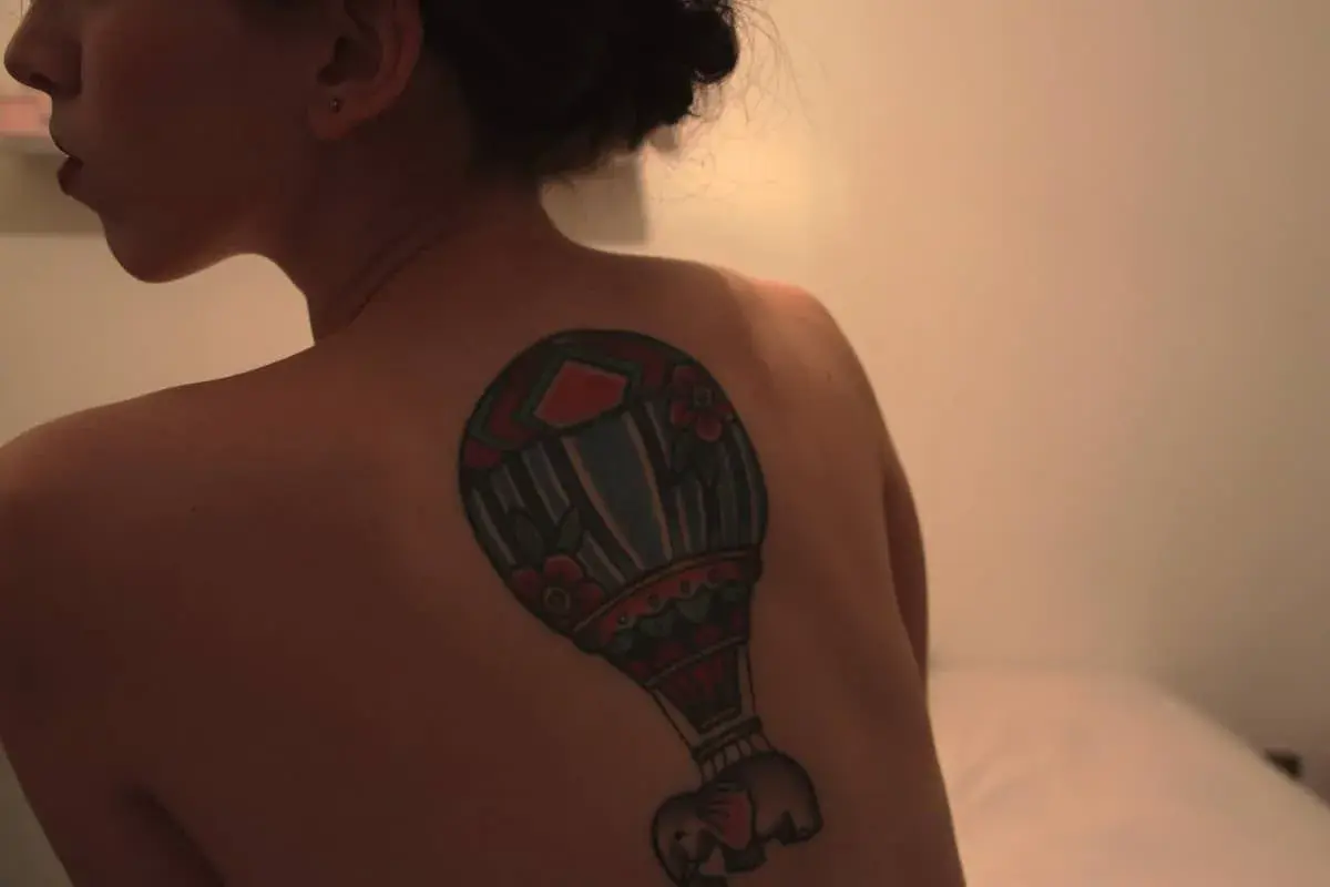 Kolorowy tatuaż balon z małym słoniem na plecach kobiety.