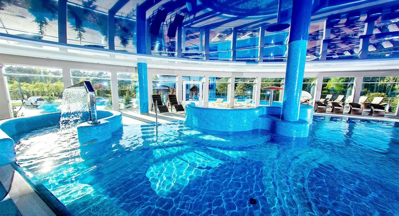 Relaks w spa nad morzem z basenem. Woda kaskadowo spływa do błękitnego basenu, a przez panoramiczne okna widać zieleń.