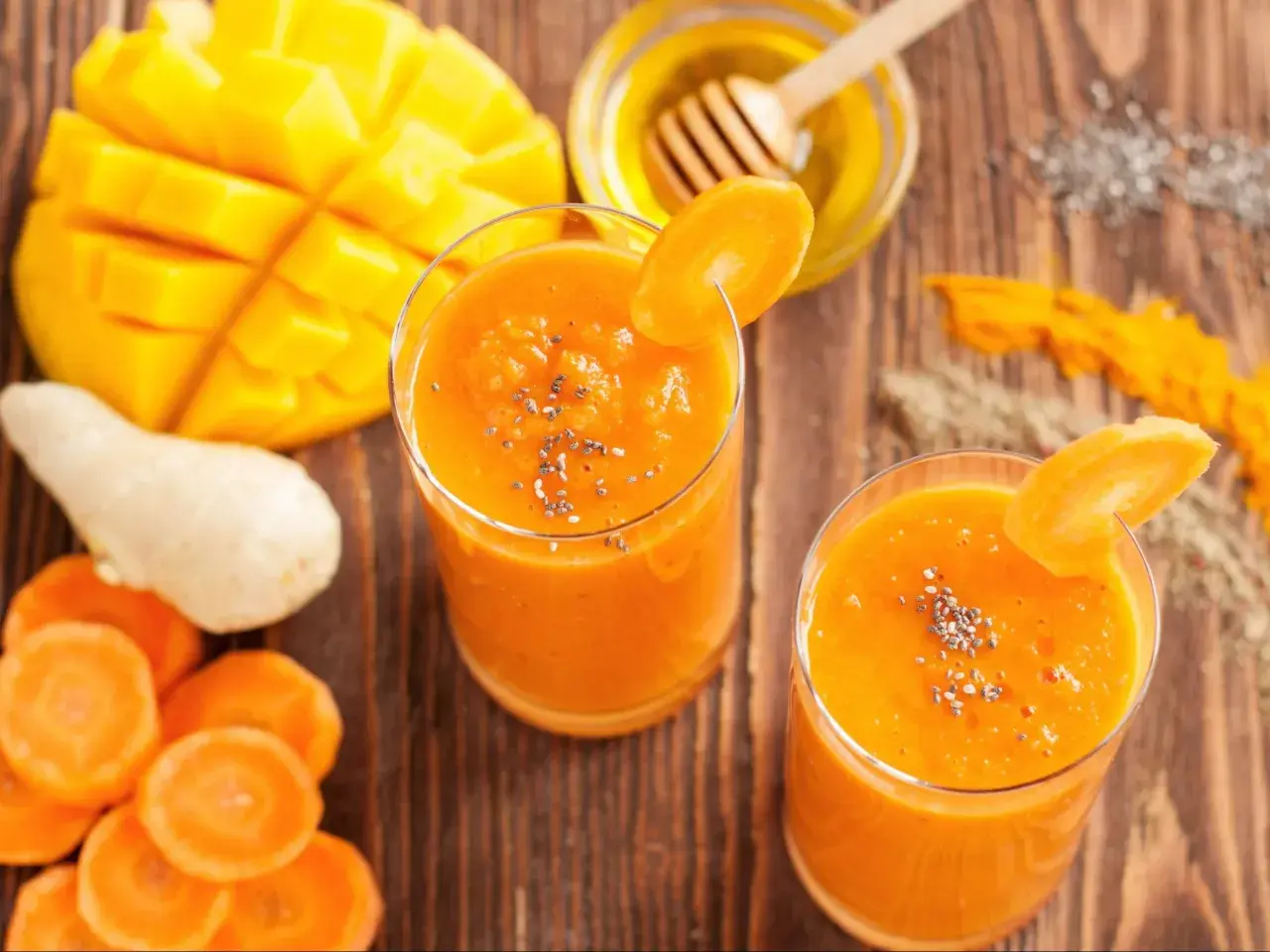 Dwa szklanki pomarańczowego koktajlu z mango i marchewki, ozdobione plasterkiem marchewki i nasionami chia.