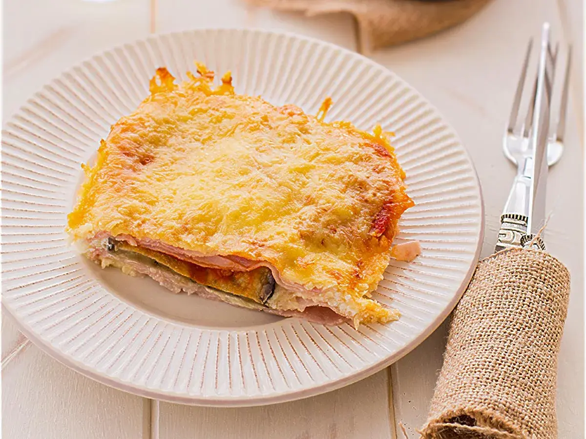 Porción de pastel de berenjenas gratinado con queso dorado, servido en plato blanco.