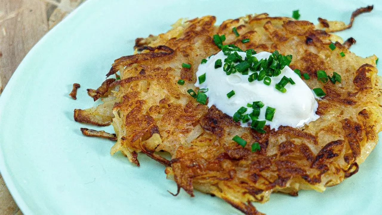 Une galette de pomme de terre dorée et croustillante, garnie d'une cuillère de crème fraîche et de ciboule ciselée. Un délice simple et savoureux.