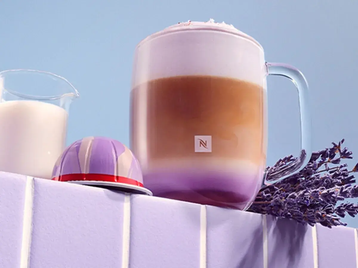 Ein aromatischer Lavendel Latte in einem Glasbecher, daneben eine Kaffeekapsel und Milch.