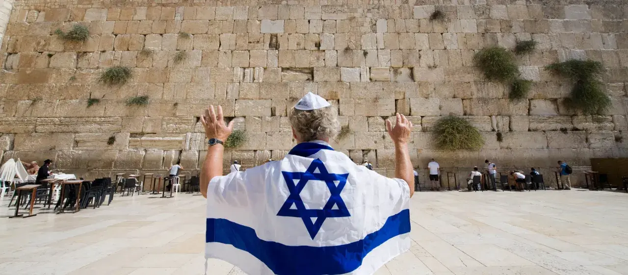 Mann mit israelischer Flagge und Davidstern betet an der Klagemauer, ein Ort des Judentums in Israel.