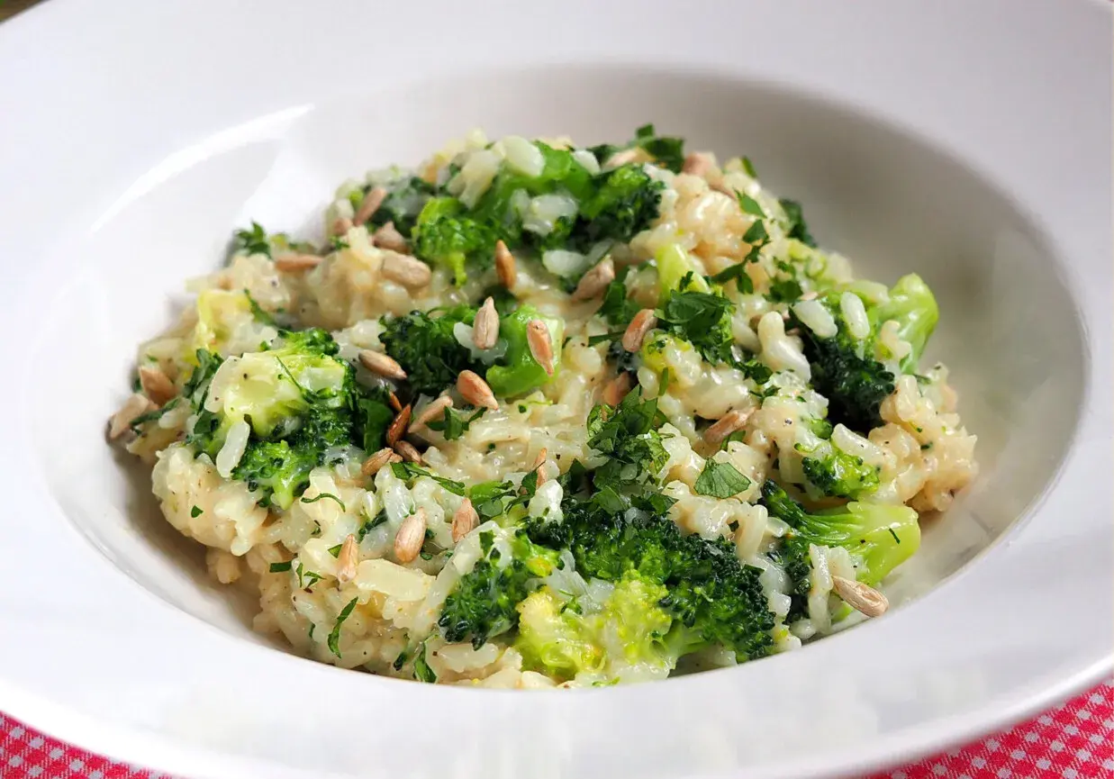 Kremowe risotto z brokułami, posypane słonecznikiem i natką pietruszki, podane w białej misce.