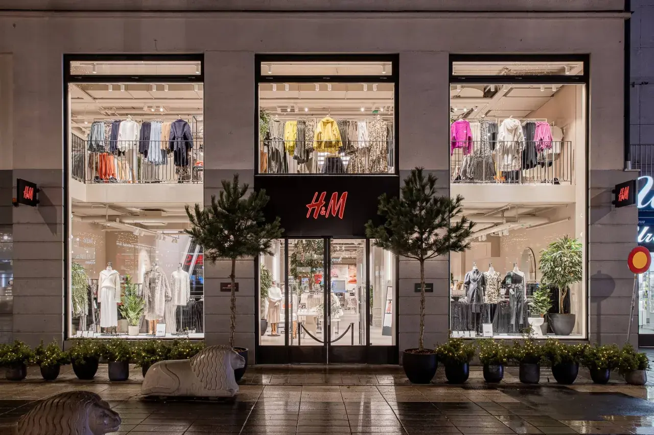 H&M-Filiale bei Nacht. Die Schaufenster zeigen Kleidung, die das Konzept von H&M als Fast Fashion widerspiegelt.
