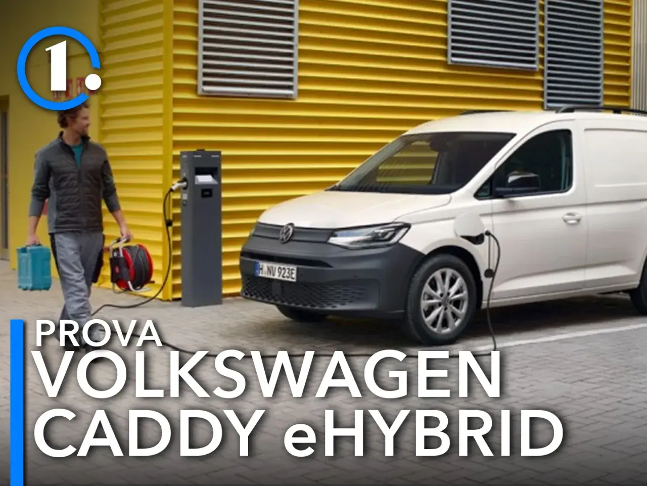 Un uomo porta cavi per caricare il Volkswagen Caddy eHybrid, un furgone bianco parcheggiato vicino a una stazione di ricarica.
