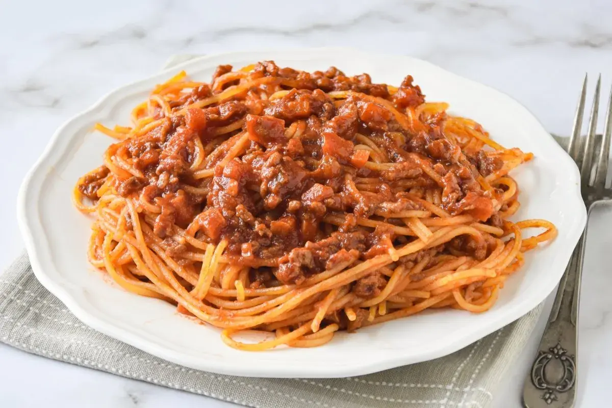Un plato de espaguetis con carne picada, cubierto con una rica salsa de tomate y trozos de carne.