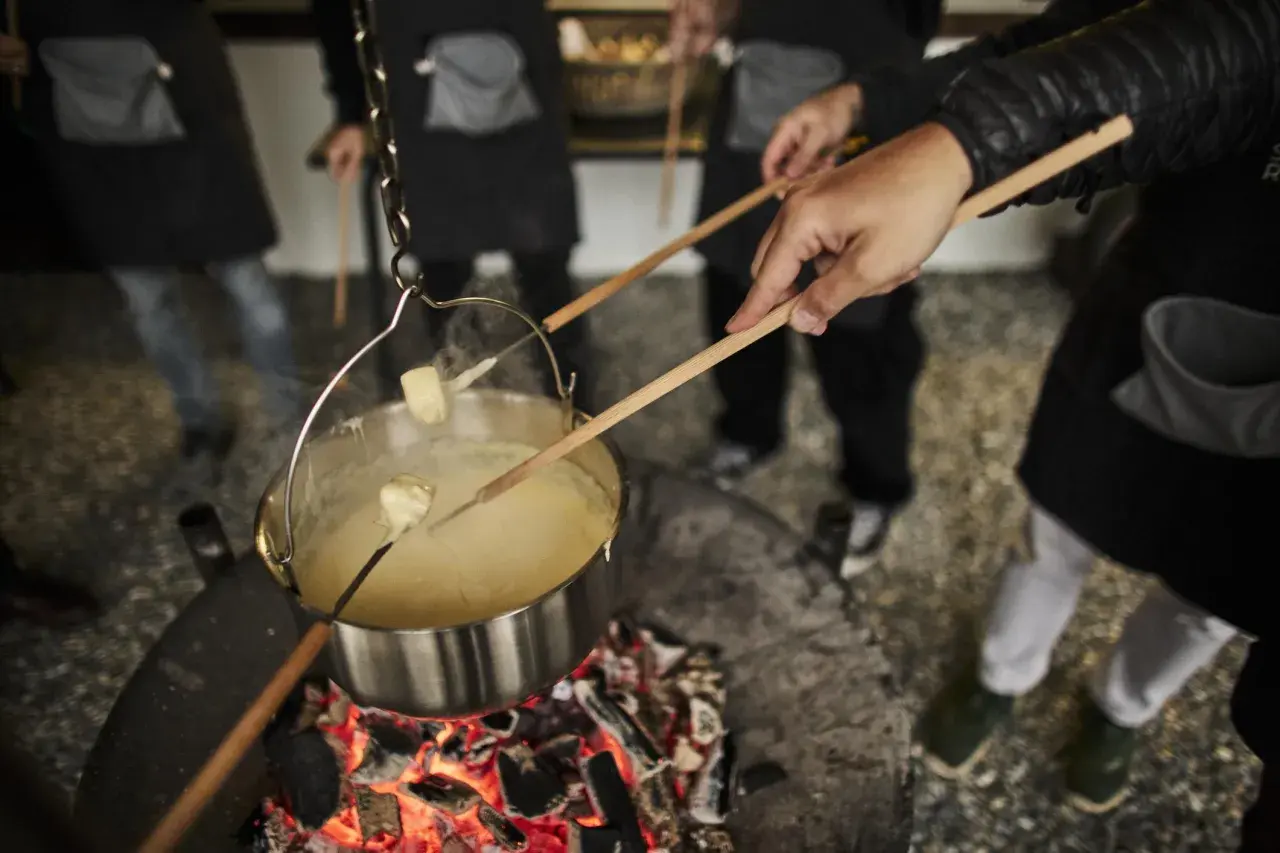 Des morceaux de pain trempent dans un caquelon de fondu suisse fumant, chauffé au-dessus d'un feu de bois.