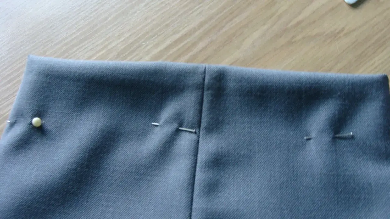 Szare spodnie z zaznaczonymi zaszewkami, gotowe do szycia. Szpilki trzymają materiał.