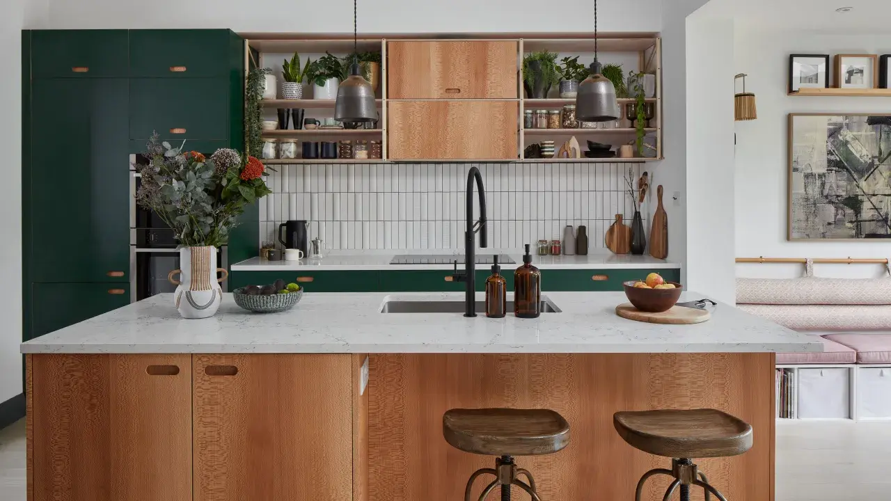 A modern kitchen island with wood grain cabinets and a white countertop, showcasing thoughtful kitchen styling with plants, fruit, and decorative items.