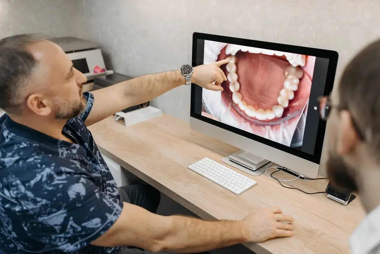 Dentysta pokazuje pacjentowi na monitorze zdjęcie jamy ustnej, wskazując na problem, jak boli kieszonka dziąsłowa.