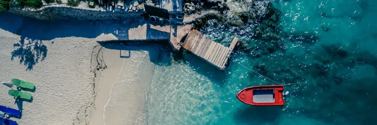 Traumhafte reiseziele august: Sandstrand, Holzsteg und ein rotes Boot im türkisfarbenen Meer. Perfekt für einen entspannten Urlaub.