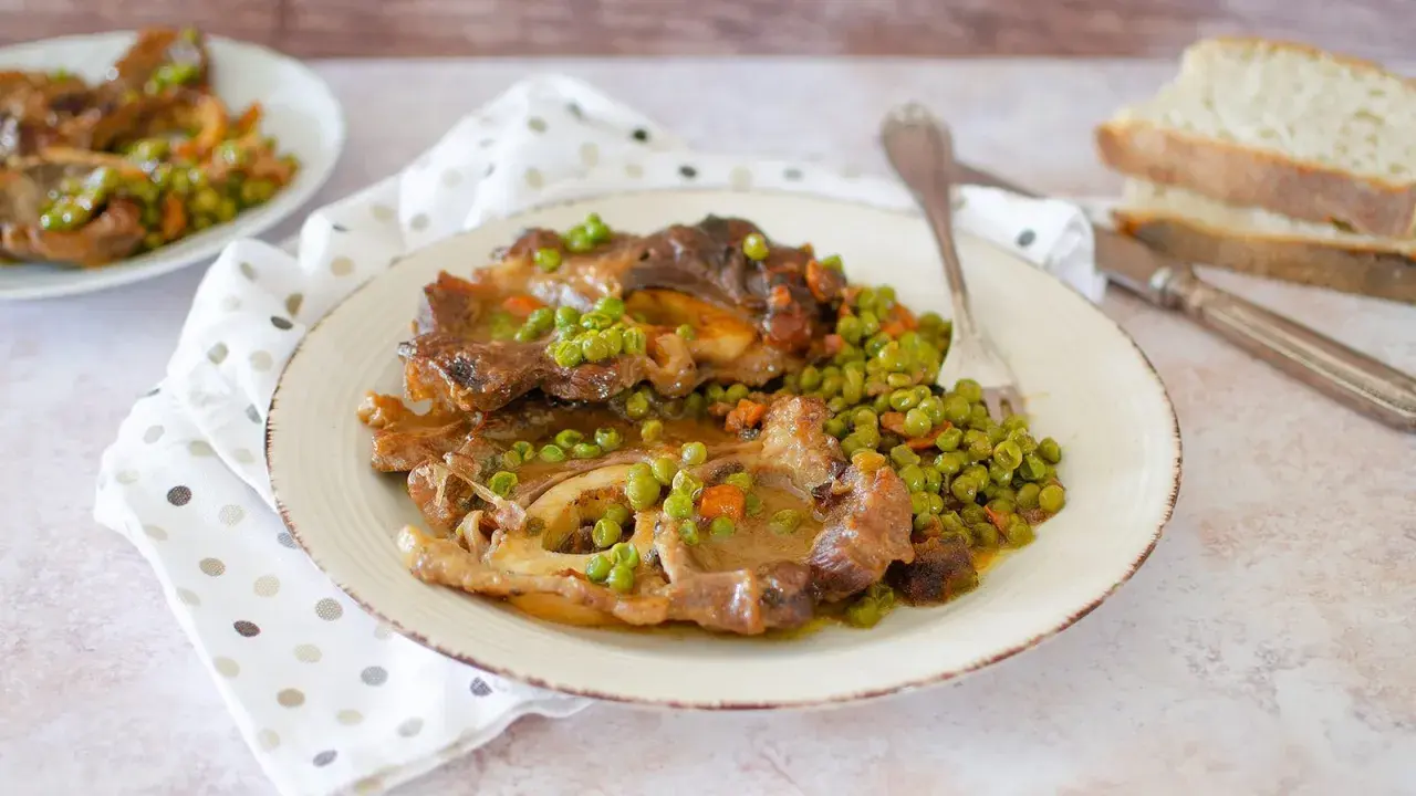 Un saporito ossobuco con piselli e carote, servito su un piatto bianco con tovagliolo a pois.