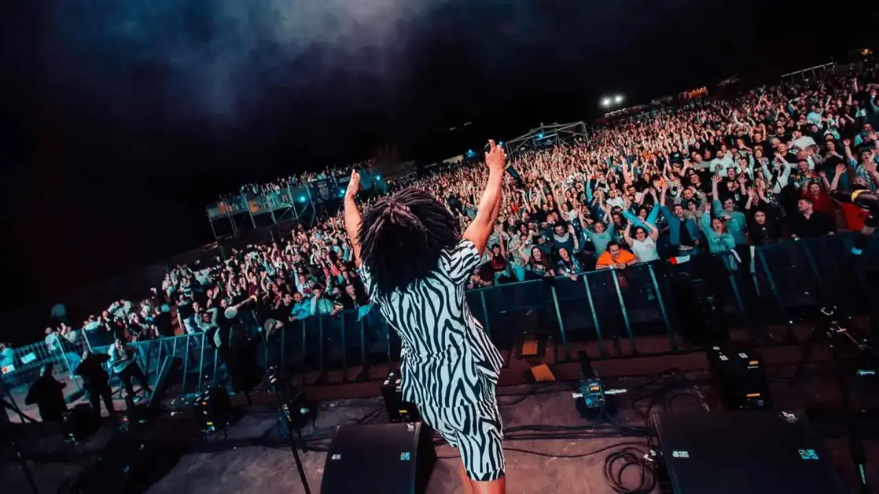 ¡Molan los 90 Zaragoza! Un artista con rastas y traje de cebra saluda a una multitud eufórica en un concierto nocturno.