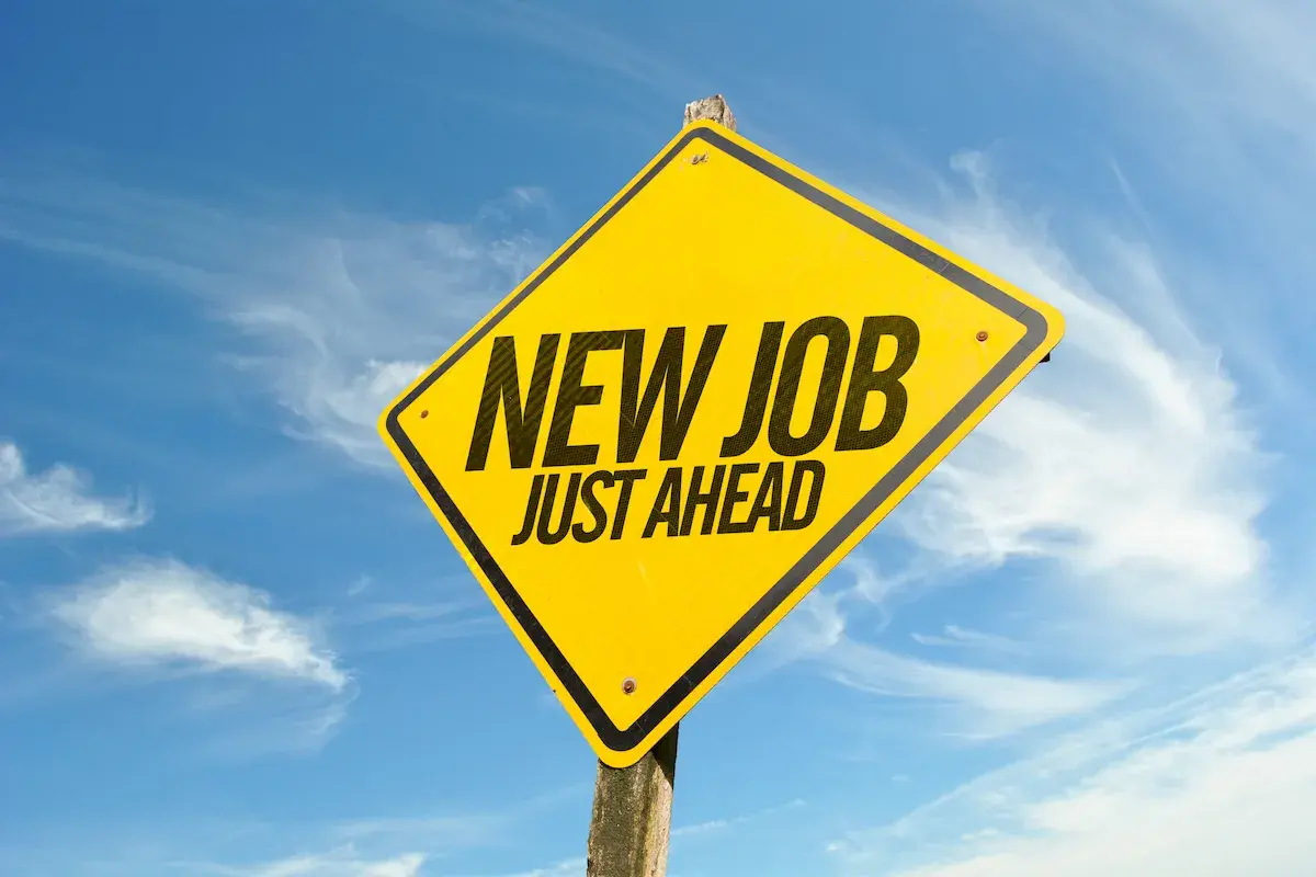 Gul varningsskylt med texten "NEW JOB JUST AHEAD" mot en blå himmel med moln. Perfekt för den som trivs inte på jobbet och söker nya utmaningar.