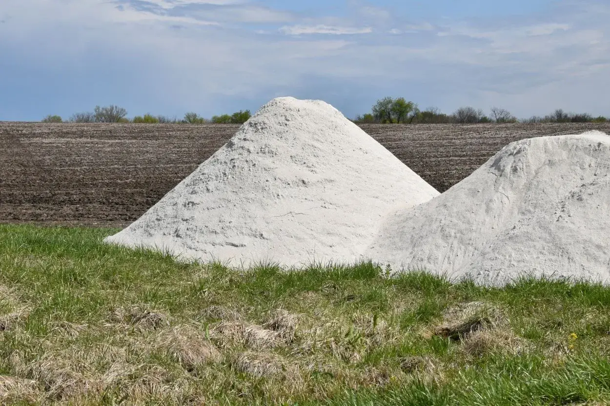Zwei große Haufen weißes Material, vielleicht Kalkstickstoff, liegen auf einem Feld. Der **Kalkstickstoff Verbot** könnte die Ursache für diese Lagerung sein.