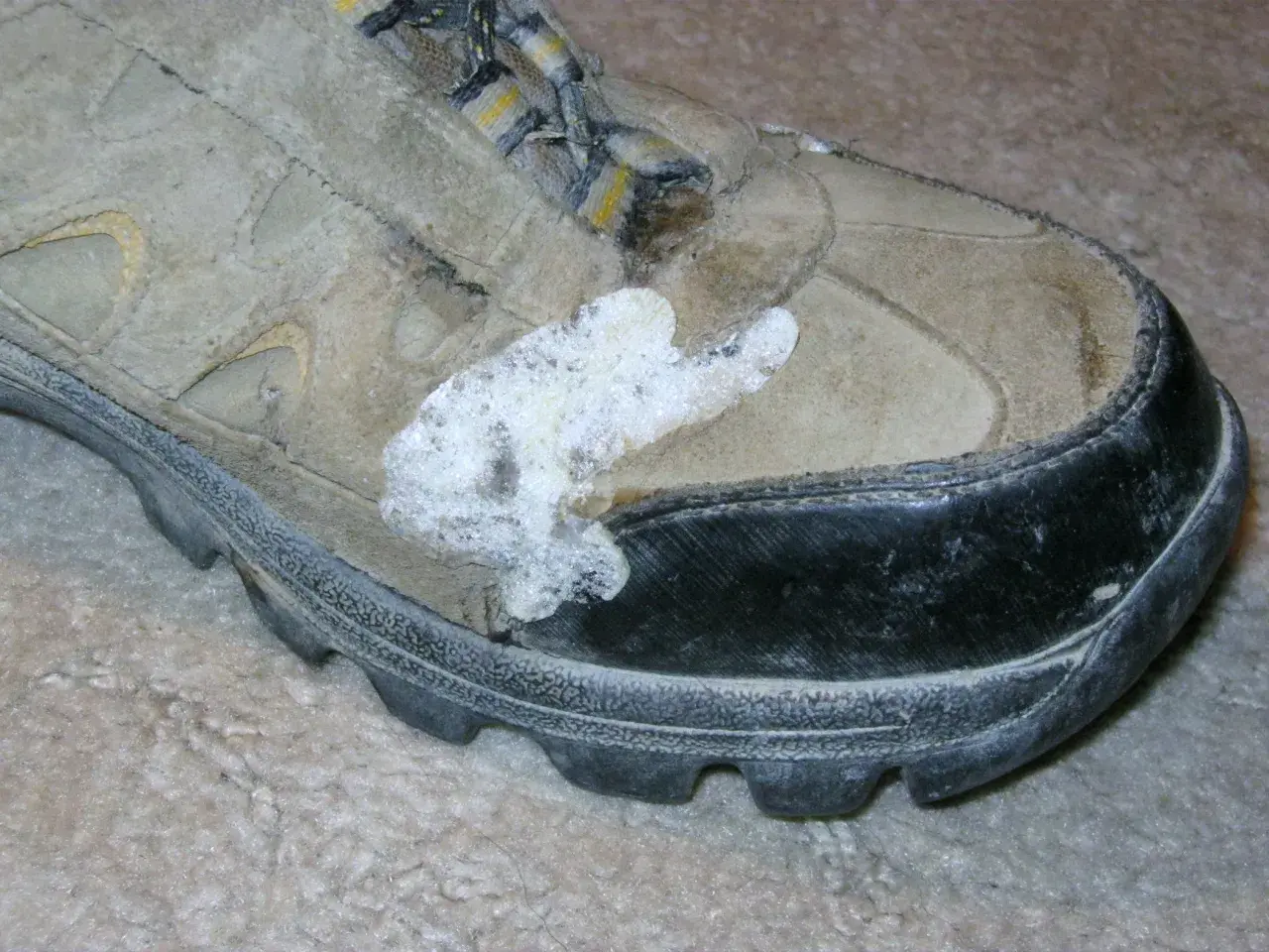 A dirty hiking boot with a white, foamy substance stuck to the side, possibly from a failed attempt to schuhsohle kleben (glue the shoe sole).