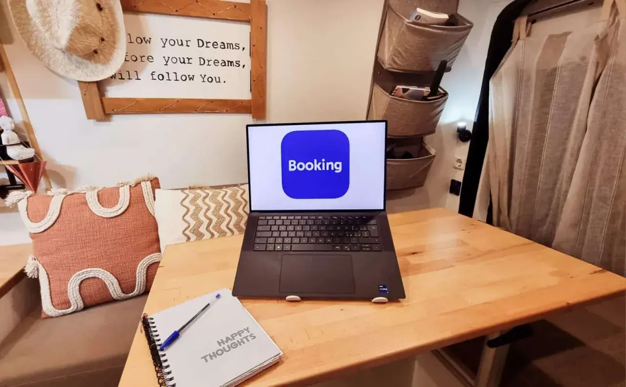 Laptop con app Booking aperta, pronto per un **instant booking** di avventure. Taccuino "Happy Thoughts" accanto.