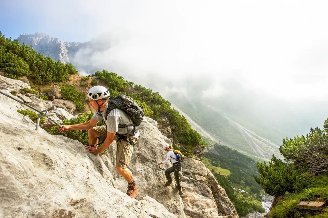 Dwóch turystów pokonuje via ferrata w Austrii, wspinając się po skalnej ścianie z ubezpieczeniem stalowej liny.