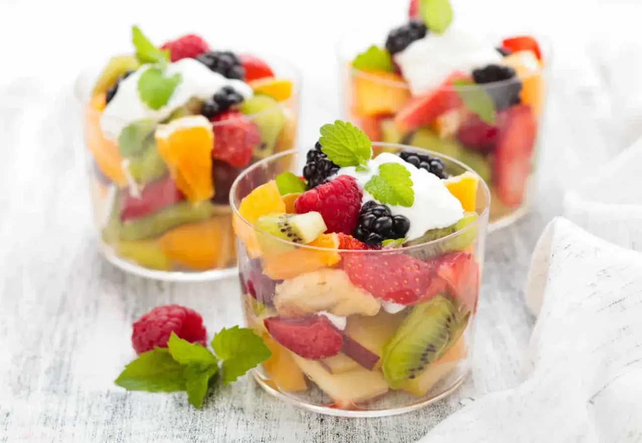 Deliciosa macedonia de frutas con fresas, kiwi, naranja, frambuesas y moras, coronada con crema y menta.