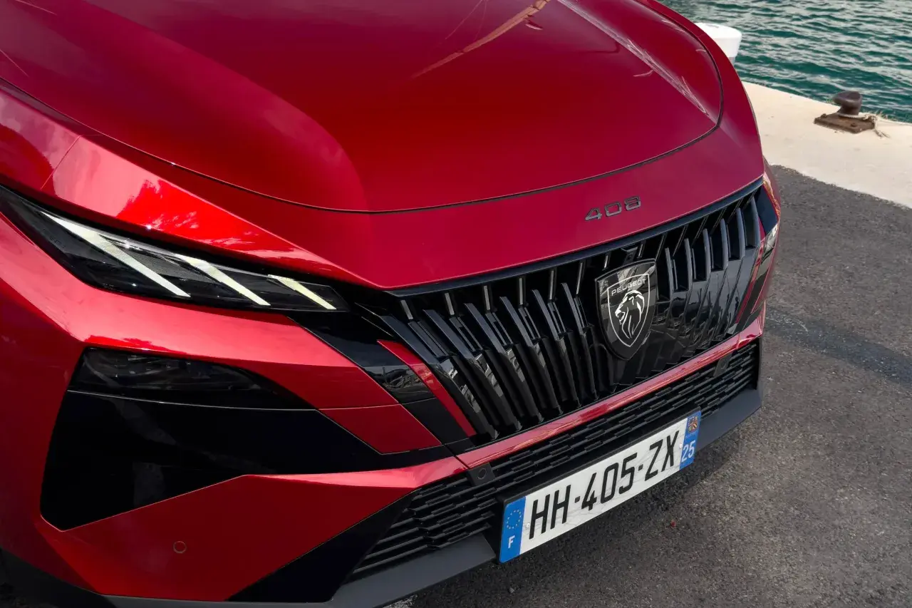 Czerwony Peugeot 408 Hybrid z charakterystycznym grillem i ostrymi światłami LED, gotowy do podróży nad wodę.