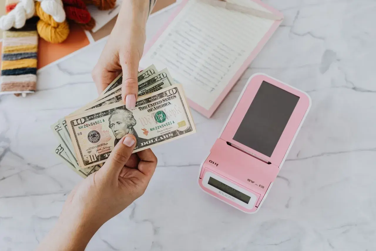 Mani che contano banconote dollari vicino a un registratore di cassa rosa. Un professionista, uno psicologo economico, analizza le spese.