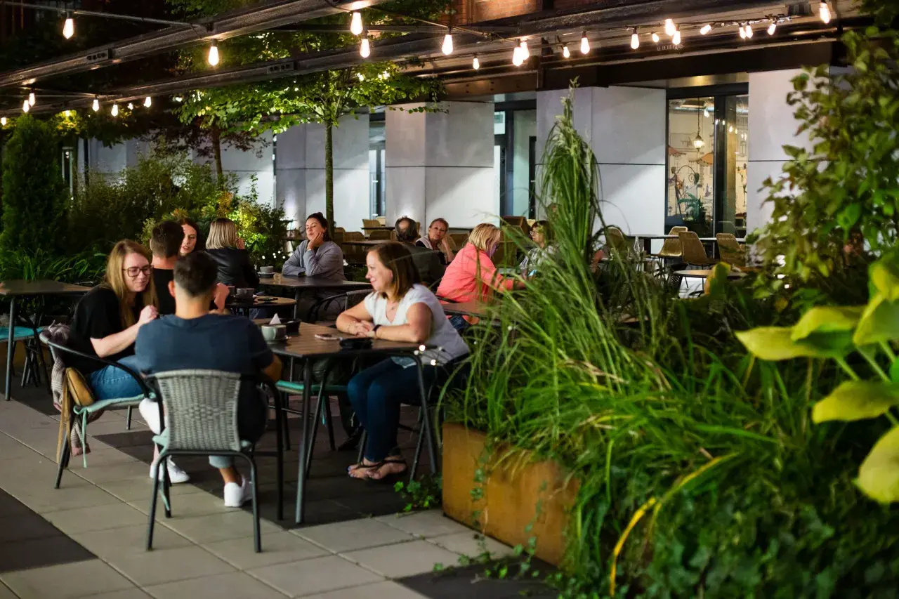 Wieczorny relaks w jednej z nowych restauracji w Łodzi. Ludzie siedzą przy stolikach, delektując się posiłkami i rozmowami.