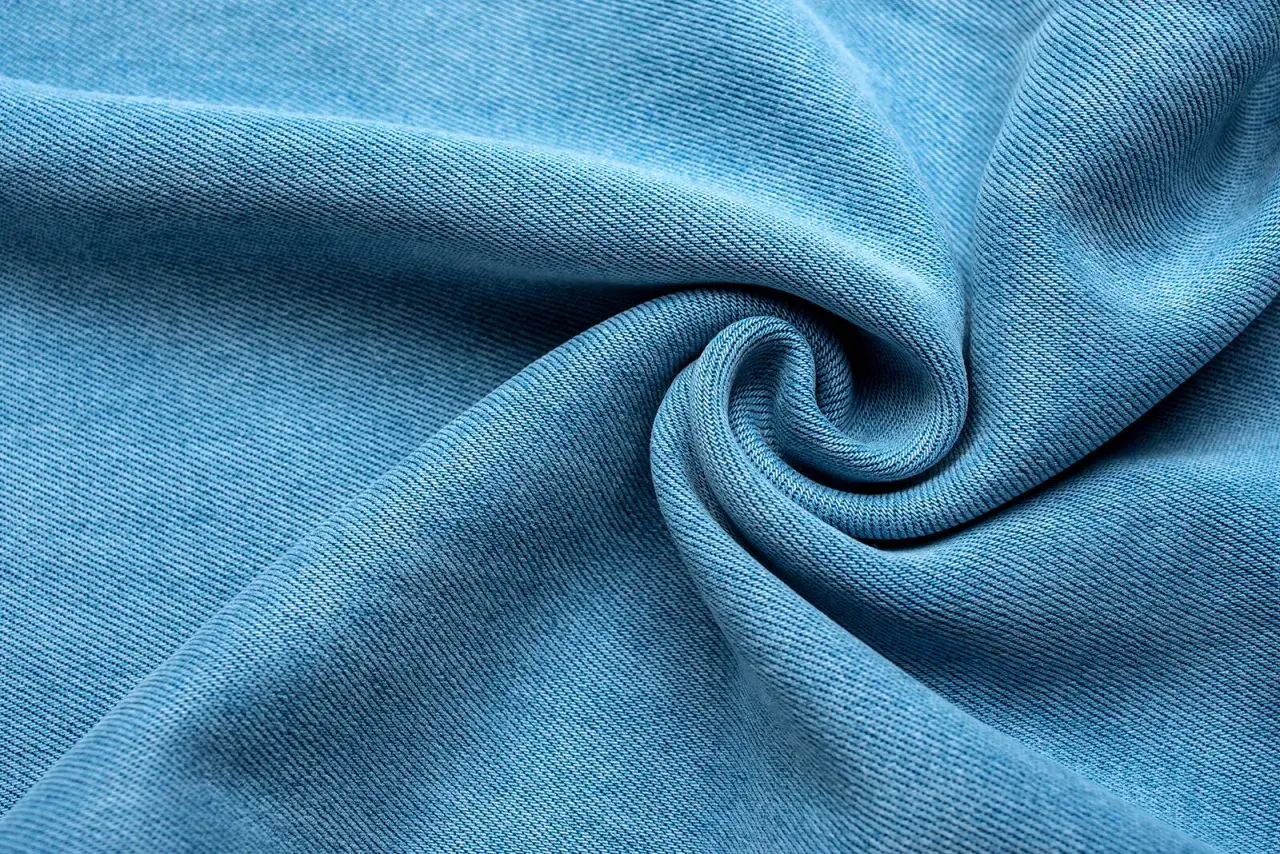 Miękka, błękitna tkanina lyocellu z charakterystycznym splotem, ułożona w eleganckie fale i spiralę.