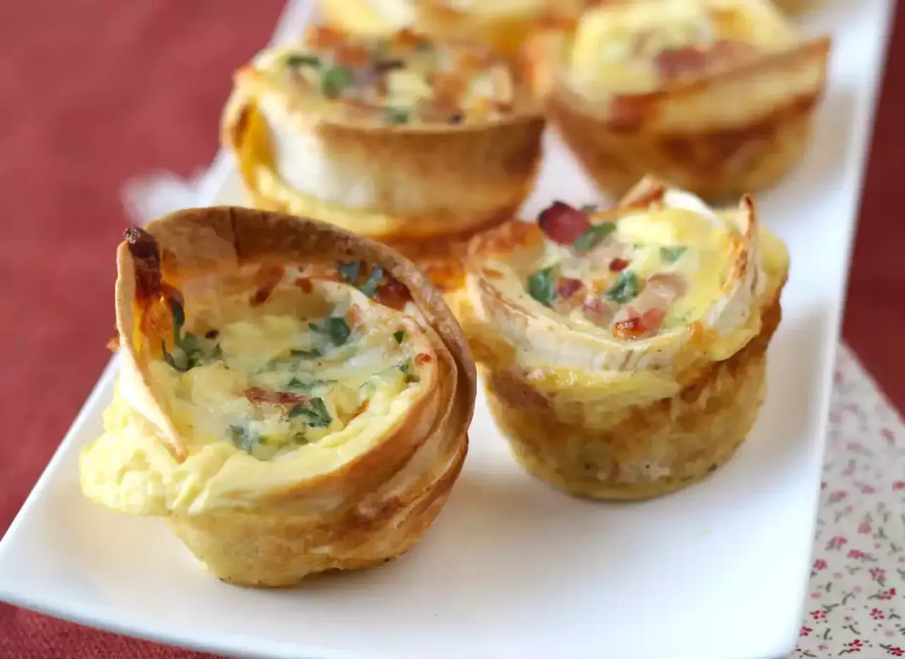 Petits quiches wraps dorés, garnis d'œufs, de lardons et de persil, servis sur une assiette blanche.